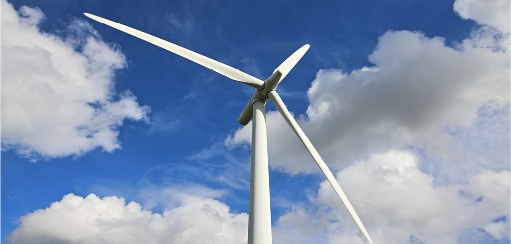 White wind turbine with three blades against a bright blue sky with fluffy white clouds.
