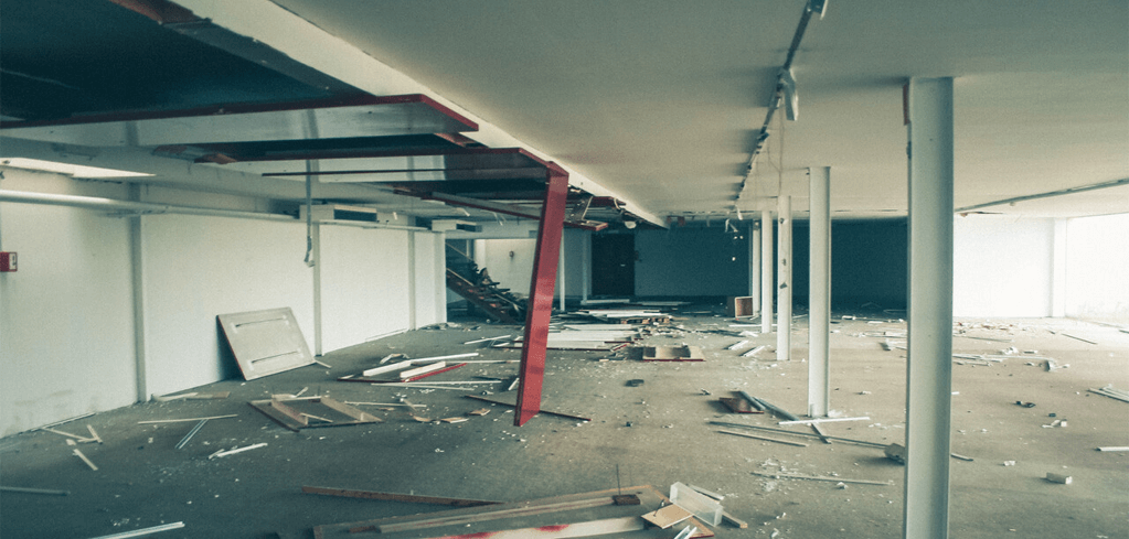 Interior of abandoned commercial space under demolition with debris scattered across floor and exposed ceiling structures.