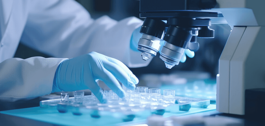 Scientist in blue gloves examining laboratory samples under a microscope in a blue-tinted laboratory setting.