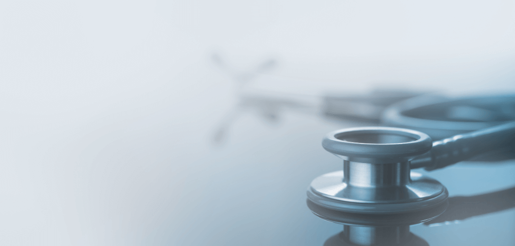 Close-up of a silver stethoscope on a blue-tinted surface with blurred medical symbol in the background.