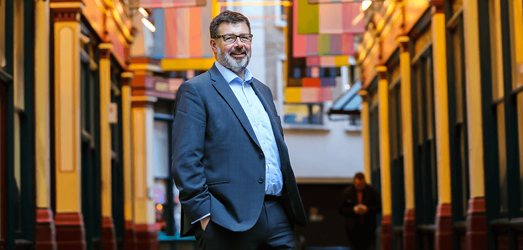 Person in blue suit standing in colorful historic arcade with yellow storefronts and decorative ceiling.