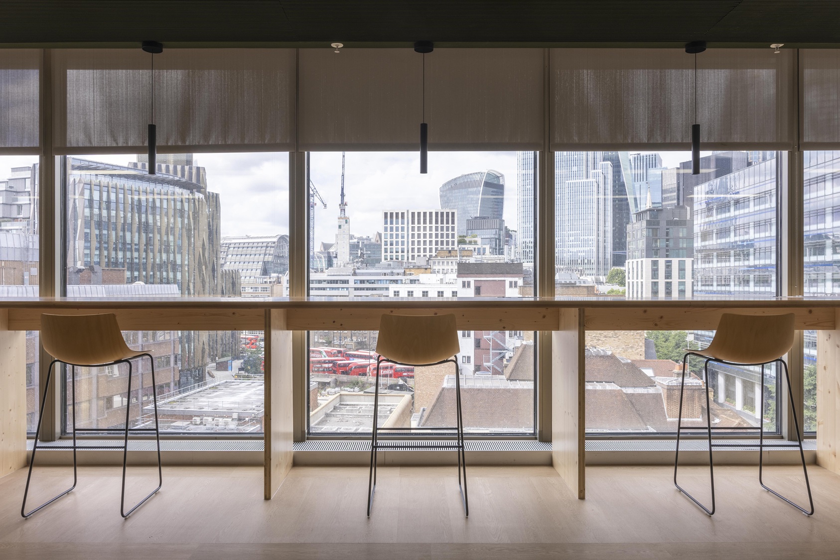Modern bar-height seating area with wooden counter facing large windows overlooking London skyline with iconic buildings.