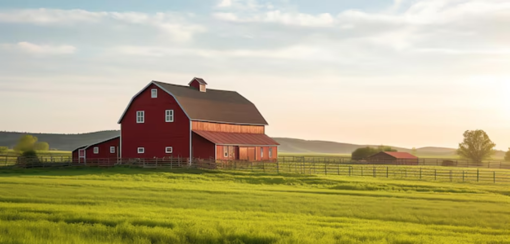 Traditional red barn with arched roof in a lush green field at sunset, rolling hills in the background under cloudy sky.