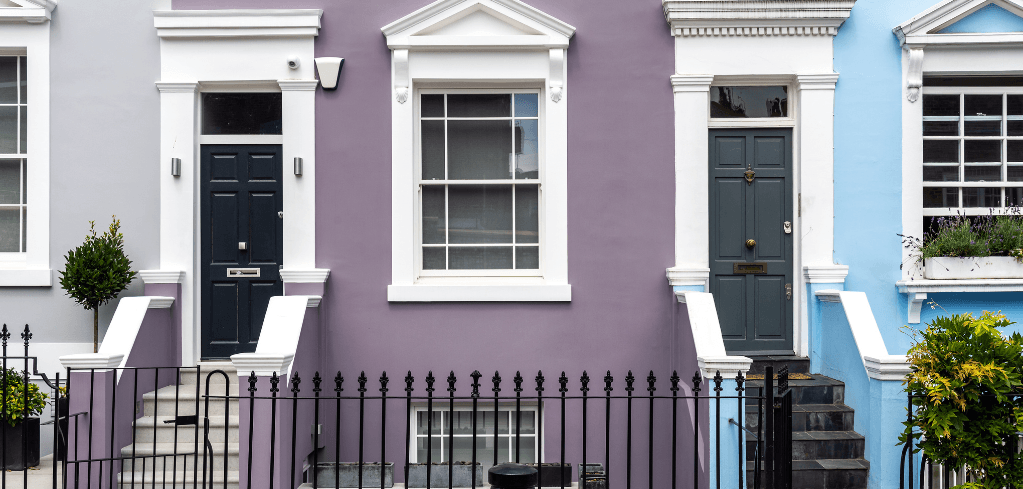 Colorful row houses with purple and blue facades, white trim, dark doors, and black iron fencing in a London neighborhood.