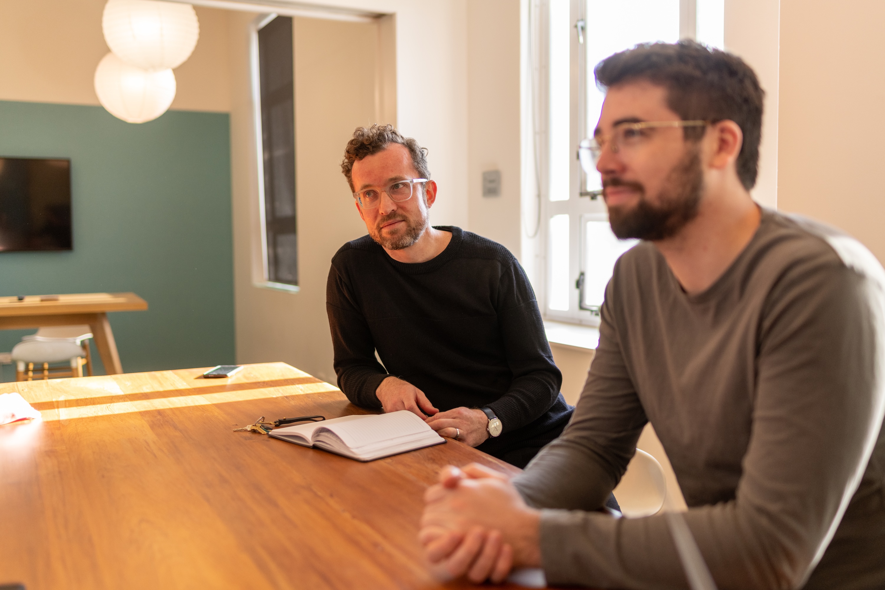 Two men at a table, one has a notebook opened in front of him