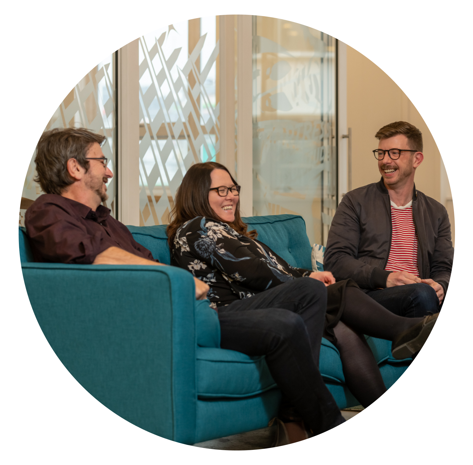 Three people smiling seated on a teal sofa