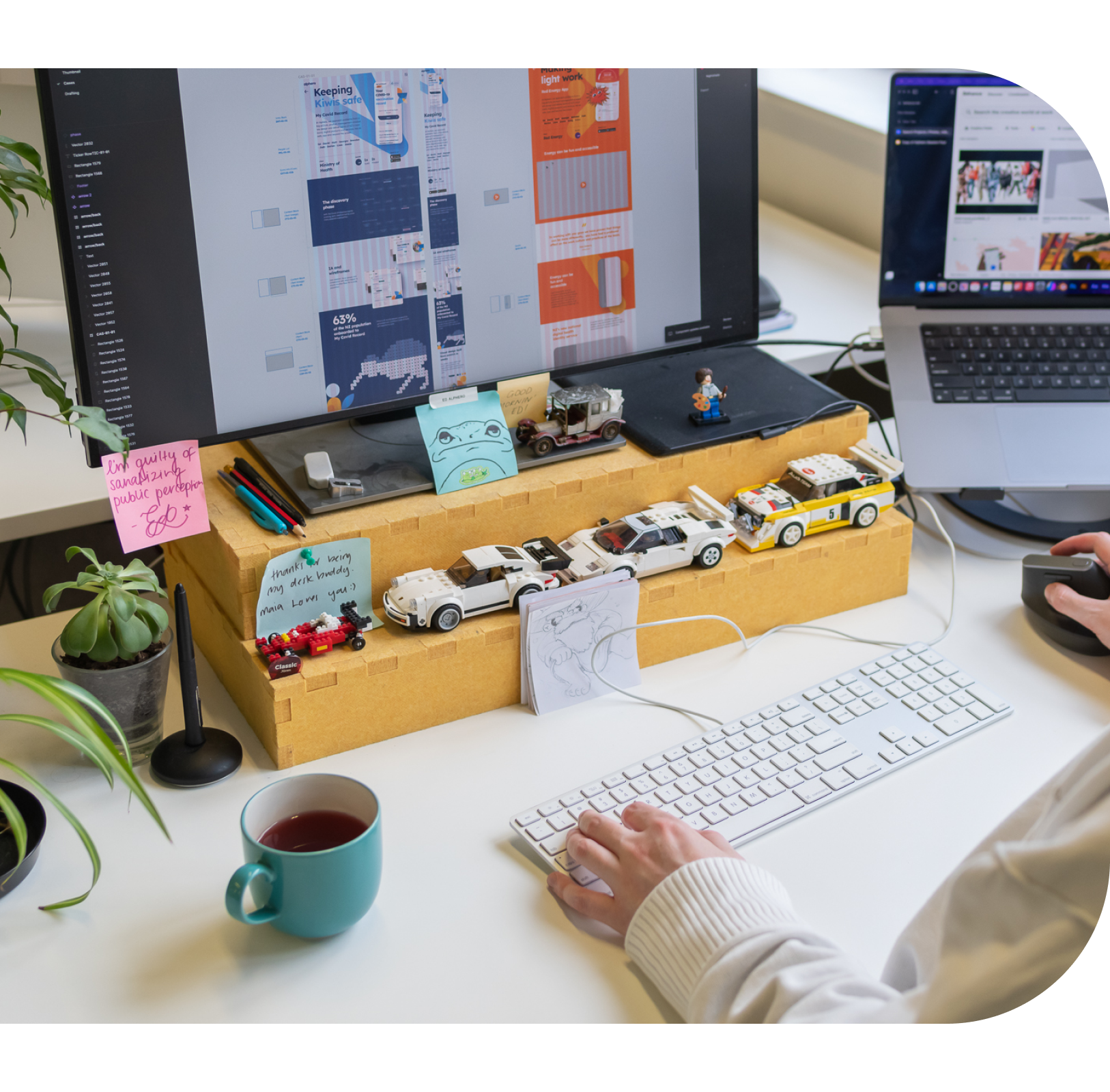 A Designer workstation that features a keyboard, monitor, toy cars and plants.