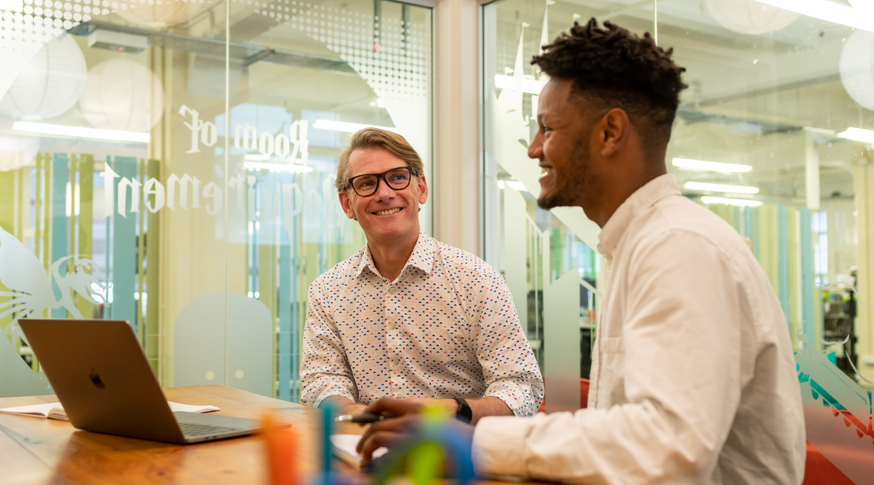 Two business men chatting and smiling in front of laptop computer