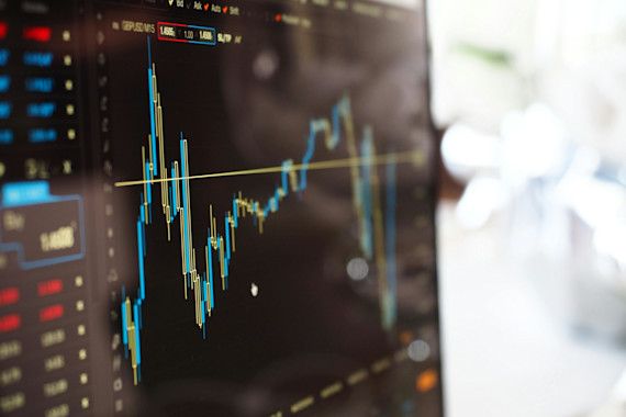 Ecrã de computador com gráfico financeiro de candlestick e dados de mercado em tempo real, representando atividade de trading ou análise de investimentos
