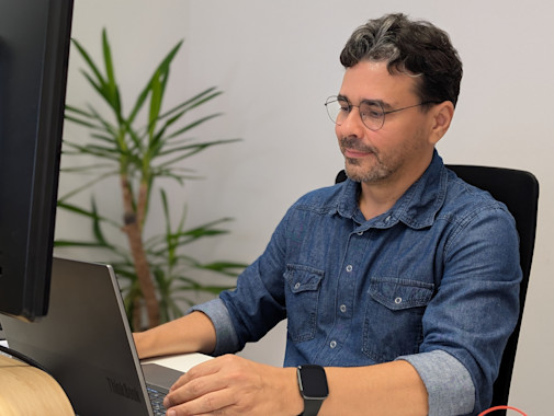 Homem a trabalhar concentrado num portátil, sentado num escritório moderno com planta decorativa ao fundo