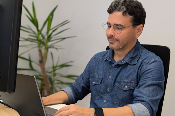 Homem a trabalhar concentrado num portátil, sentado num escritório moderno com planta decorativa ao fundo