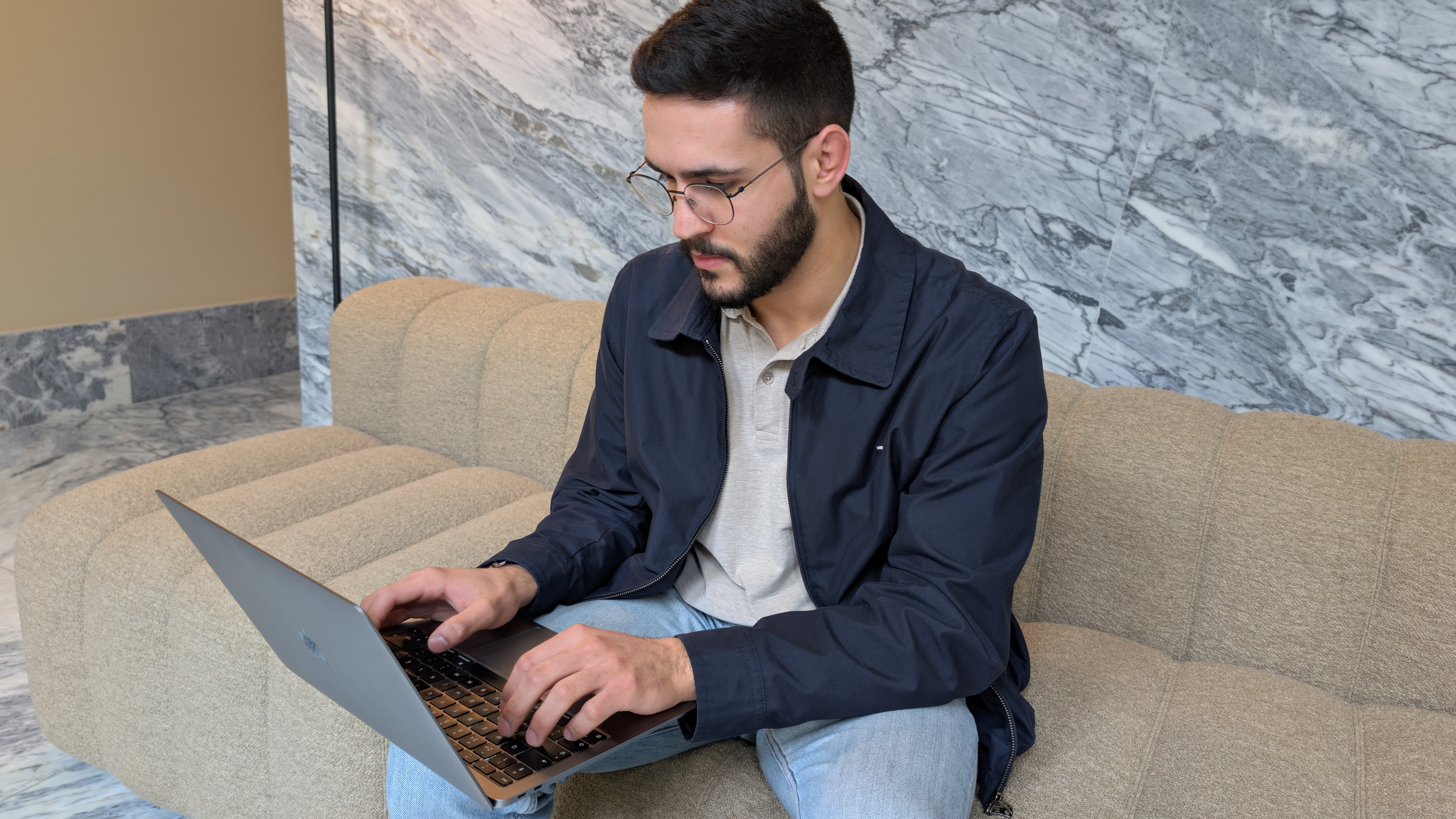 Homem sentado num sofá, a trabalhar num portátil num ambiente interior calmo e luminoso.