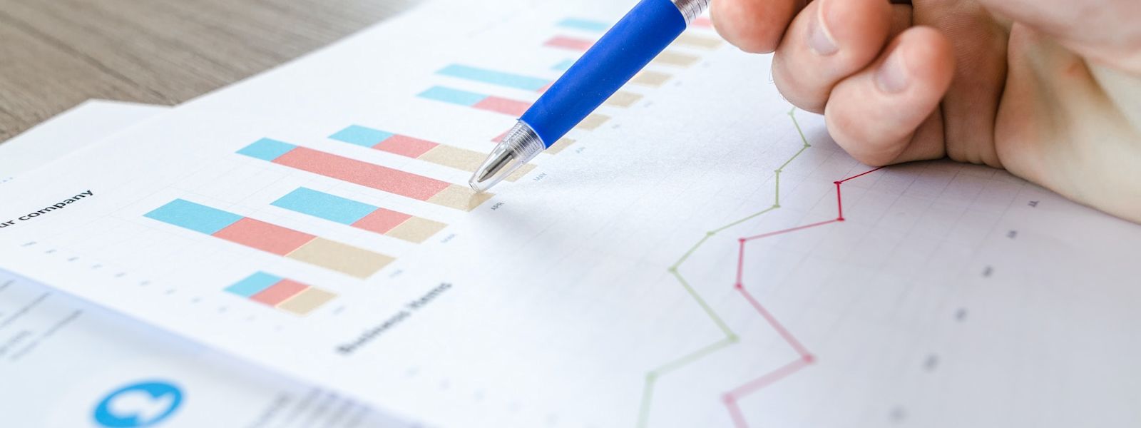 A close up of a piece of paper with a bar chart and line chart. Someone's hand is holding a blue pen and they're pointing to the bar chart.