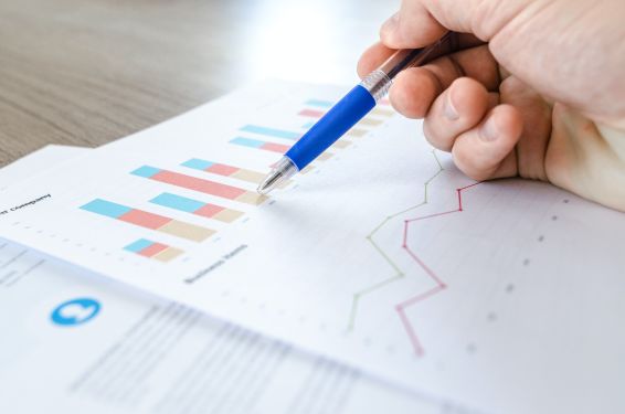 A close up of a piece of paper with a bar chart and line chart. Someone's hand is holding a blue pen and they're pointing to the bar chart.