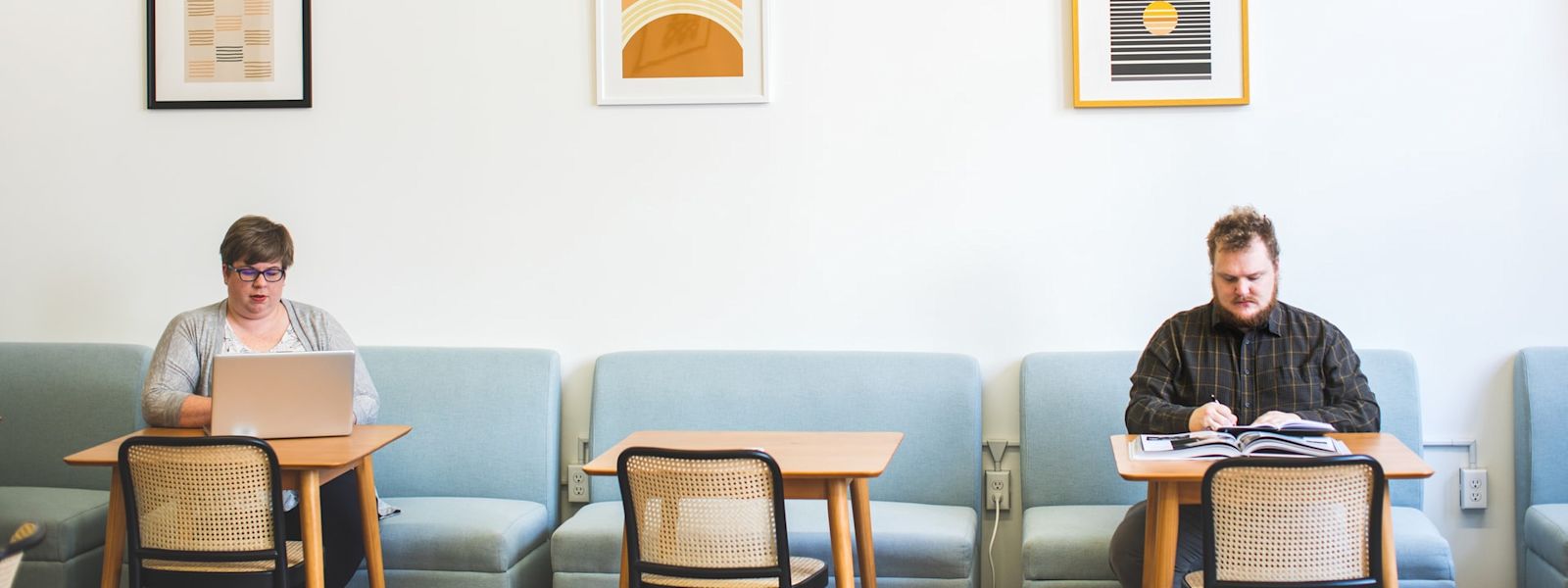 2 people are working hard, in the zone, at a cafe. One is on a laptop and the other is writing with pen and paper.