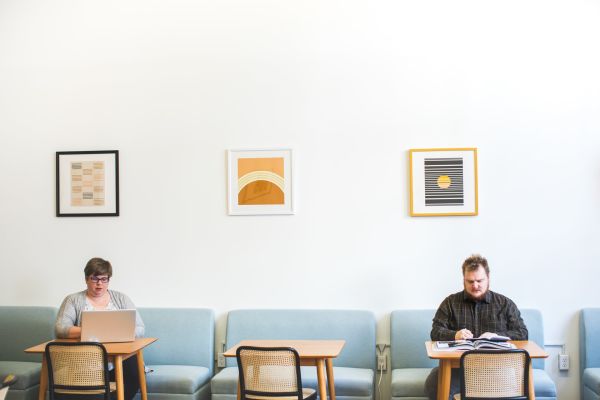 2 people are working hard, in the zone, at a cafe. One is on a laptop and the other is writing with pen and paper.