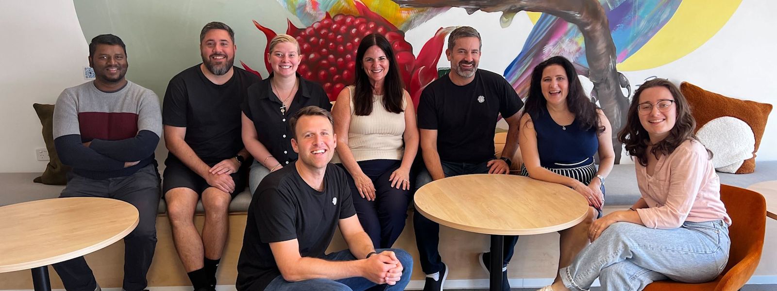 Mary with some of the Karbon Melbourne team sitting in front of a mural of rainbow birds.