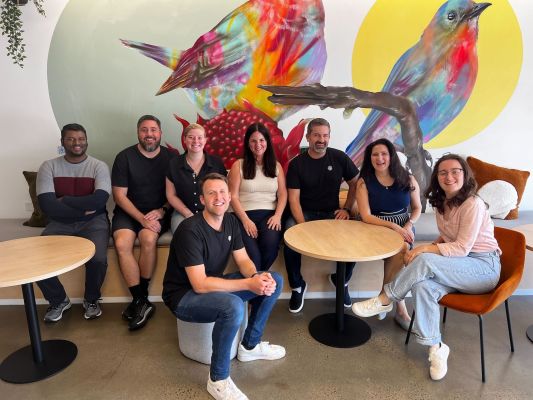 Mary with some of the Karbon Melbourne team sitting in front of a mural of rainbow birds.