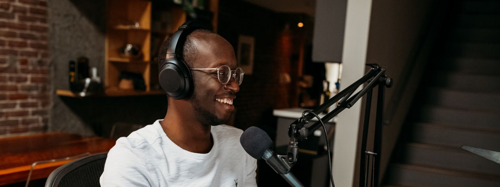 A professional podcaster in a casual white tee, engaging with his audience through a microphone in a cozy studio setting.