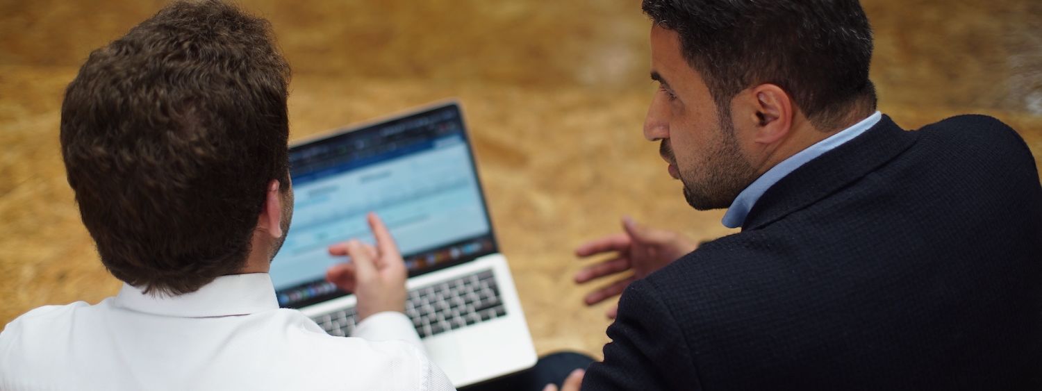 The back of two people in deep discussion, pointing to a lpatop screen.