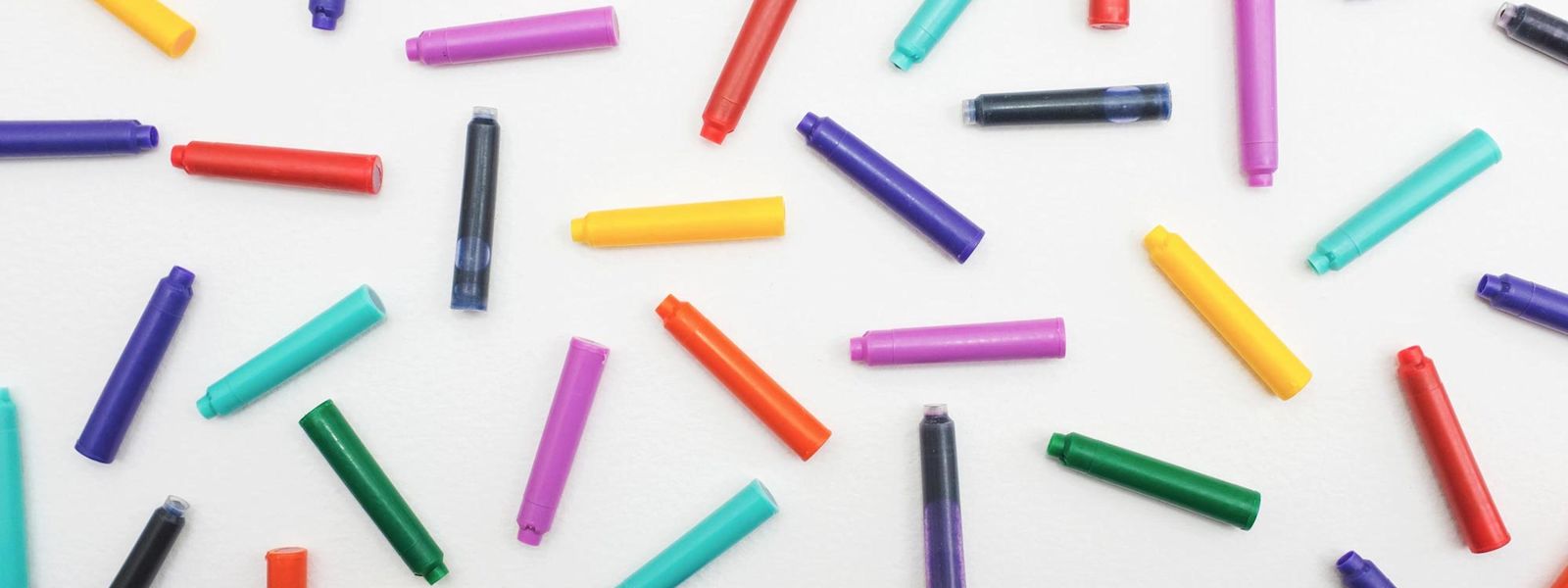 A collection of small tubes of coloured ink scattered on a flat surface.