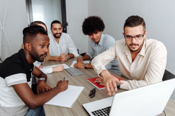 A group of colleagues all sitting around a desk, each looking intently at a laptop.