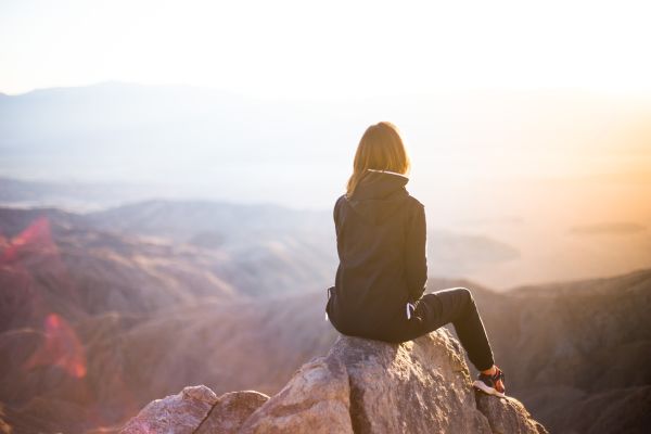 A person is sitting with their back to the camera on a rock and looking out over an expansive view of a rock formation.