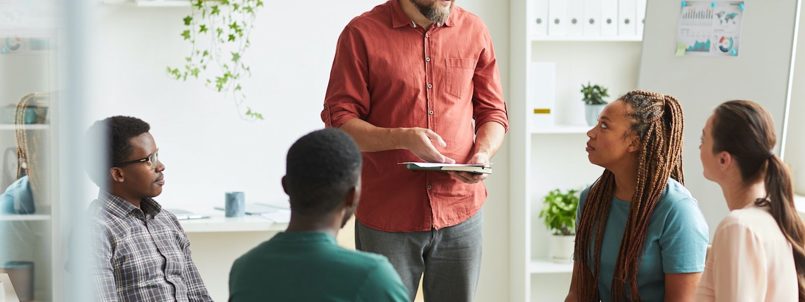 Over-communicating at your accounting firm is a sign of good leadership. A group of people are huddled around at the office, with one person standing up and leading the conversation.