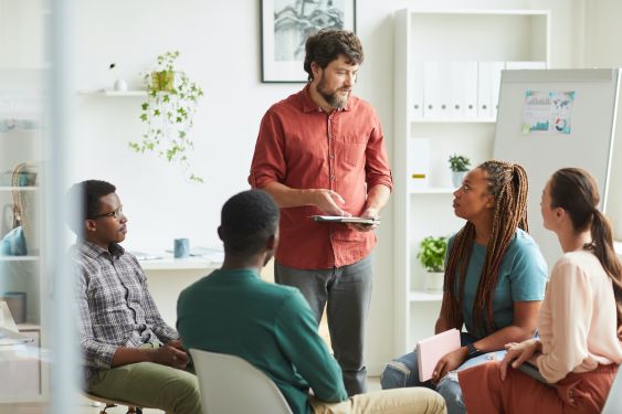 Over-communicating at your accounting firm is a sign of good leadership. A group of people are huddled around at the office, with one person standing up and leading the conversation.