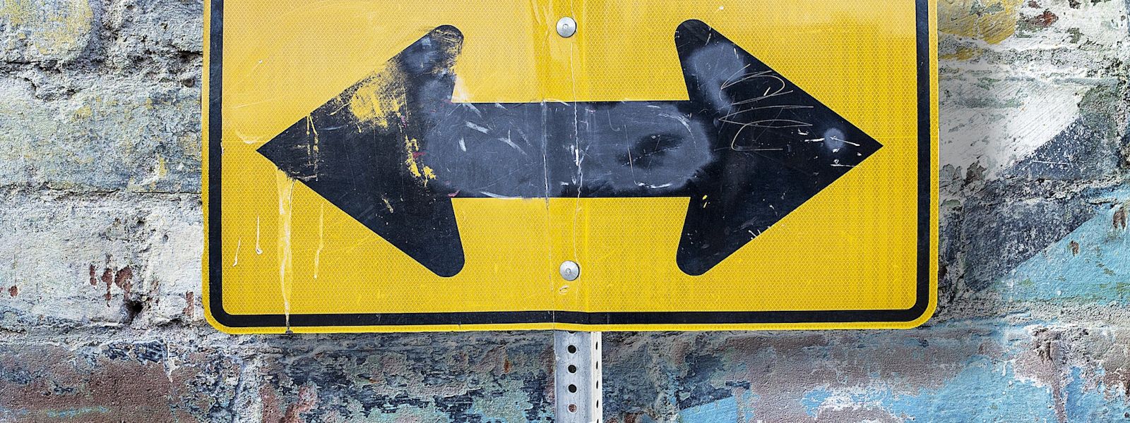 A yellow and black directional sign with 2 arrows pointing in opposite directions.