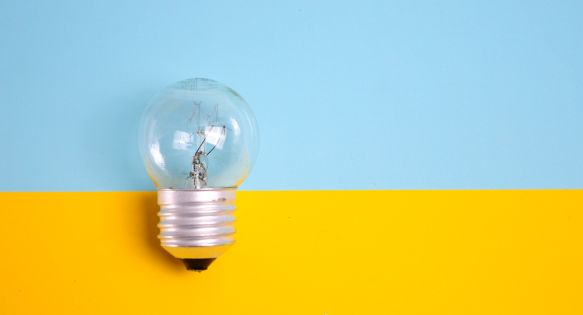 A light bulb in front of a wall that is painted light blue on the top and bright yellow on the bottom.