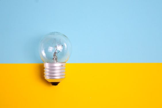 A light bulb in front of a wall that is painted light blue on the top and bright yellow on the bottom.