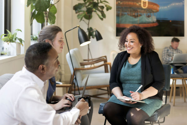 3 people are sitting on chairs, chatting and smiling.