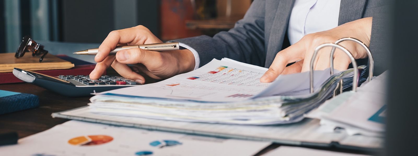 Close-up of an accountant's hands using a calculator and reviewing a colorful accounting report with graphs, reflecting the efficiency of using specialized accounting templates