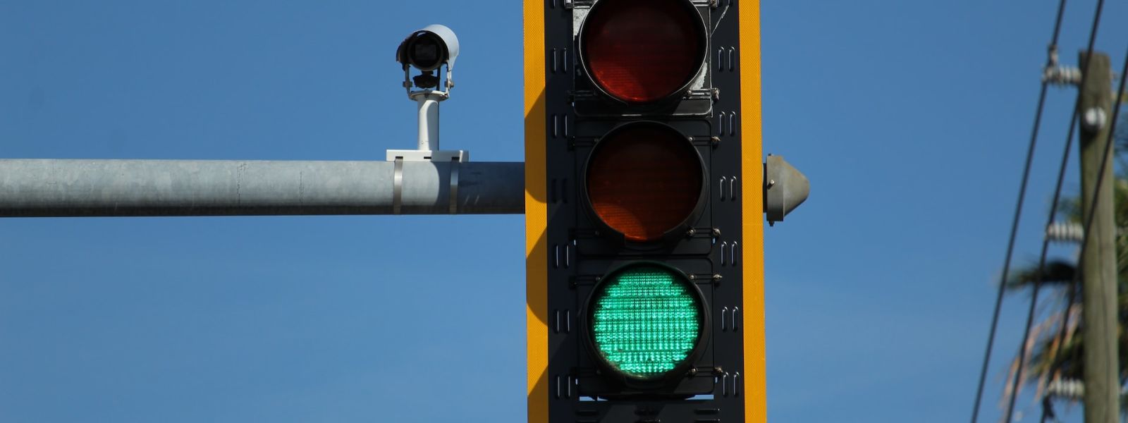 A single set of traffic lights, with the green light on. The background is a blue sky and some electrical poles and wires.