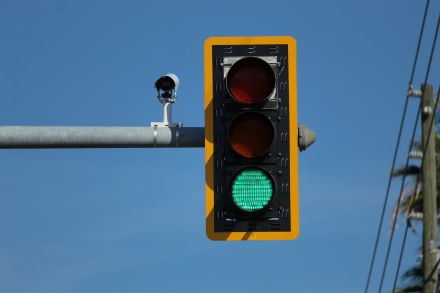 A single set of traffic lights, with the green light on. The background is a blue sky and some electrical poles and wires.