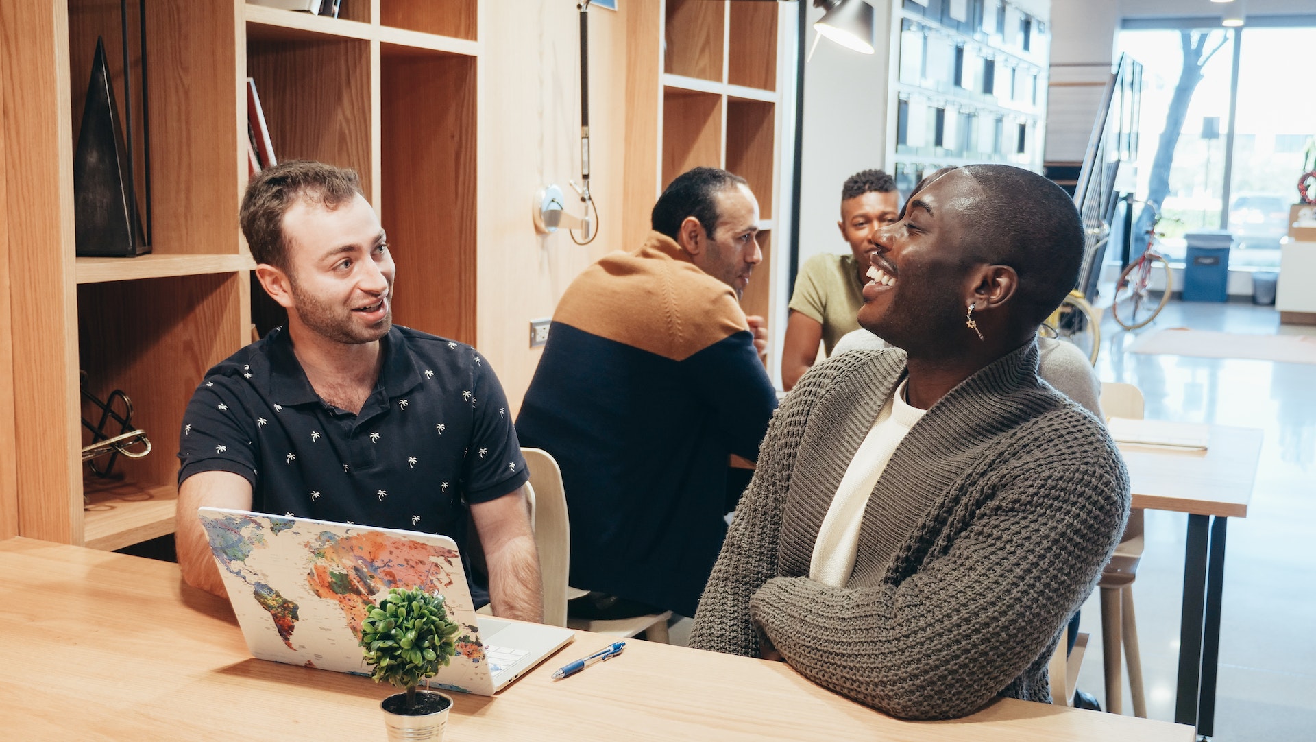 Two people sitting next to each other at a table with a laptop and fake plant. They're smiling and laughing.