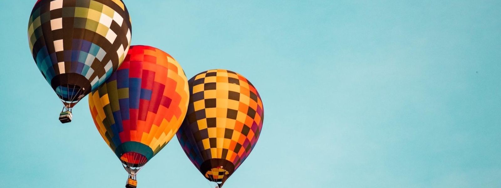 Three colorful hot-air balloons in flight in a clear blue sky.