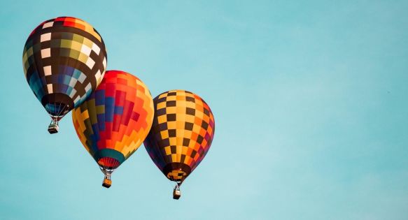 Three colorful hot-air balloons in flight in a clear blue sky.