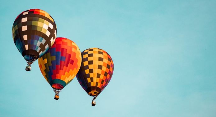Three colorful hot-air balloons in flight in a clear blue sky.