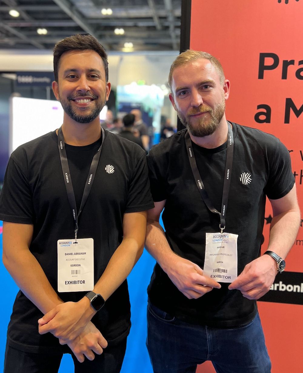 Dan Abraham and Aaron Lee standing next to each other at Accountex London 2023. They're both wearing black Karbon tshirts and the Karbon exhibition stand is in the background.