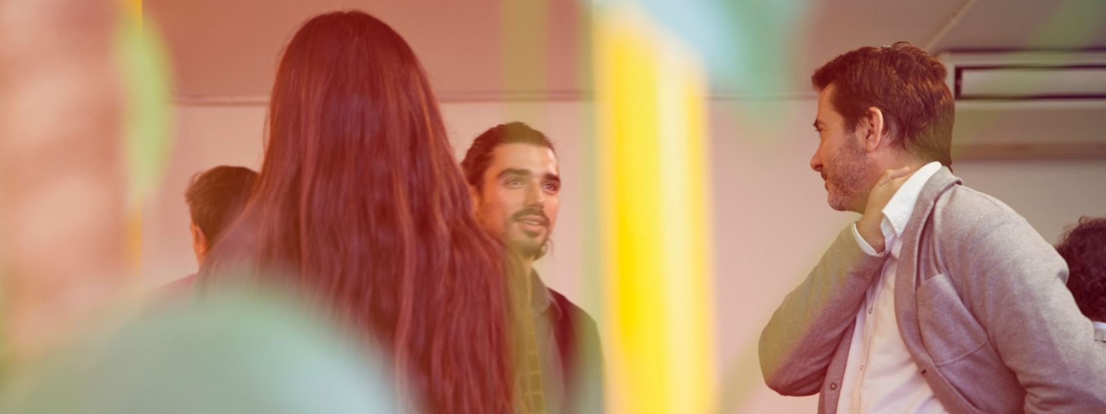 3 people in conversation, there is an indoor plant in the foreground.