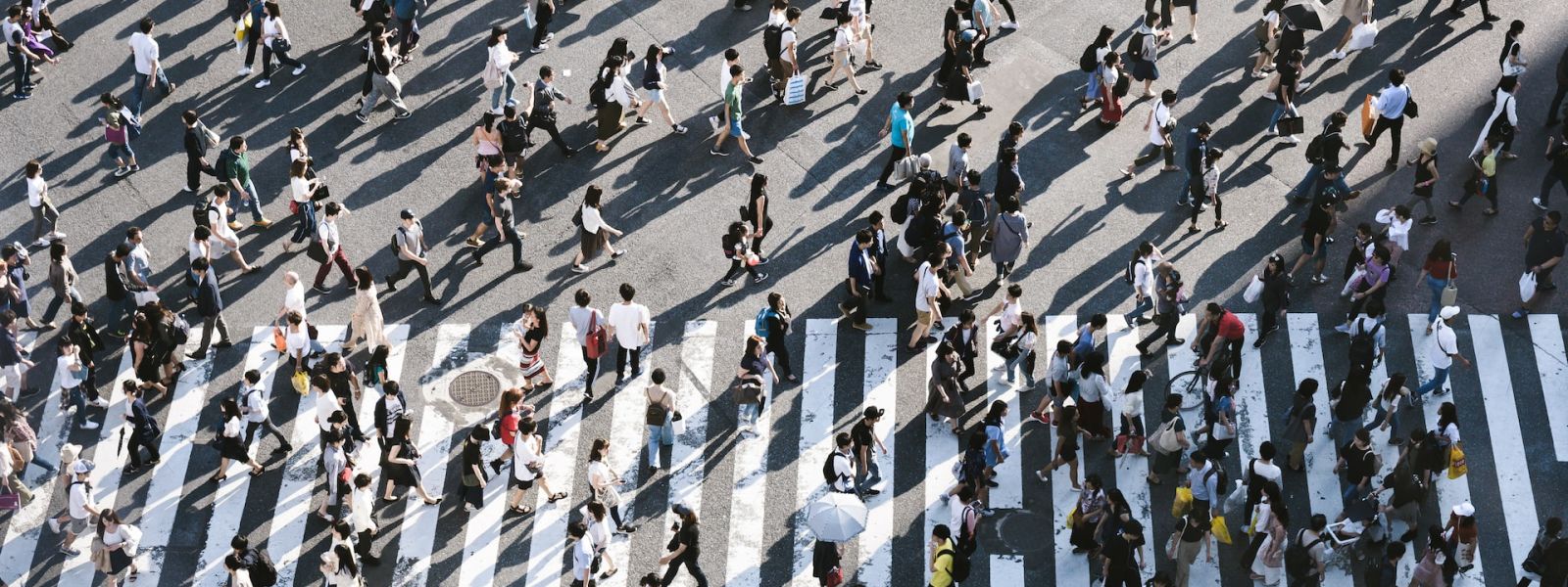 An aerial view of a busy crosswalk. People are walking in every direction, spilling out over the crossing road markings.