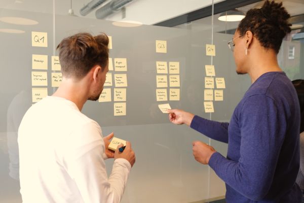 Two people are managing and planning quarterly projects using sticky notes on an internal window.