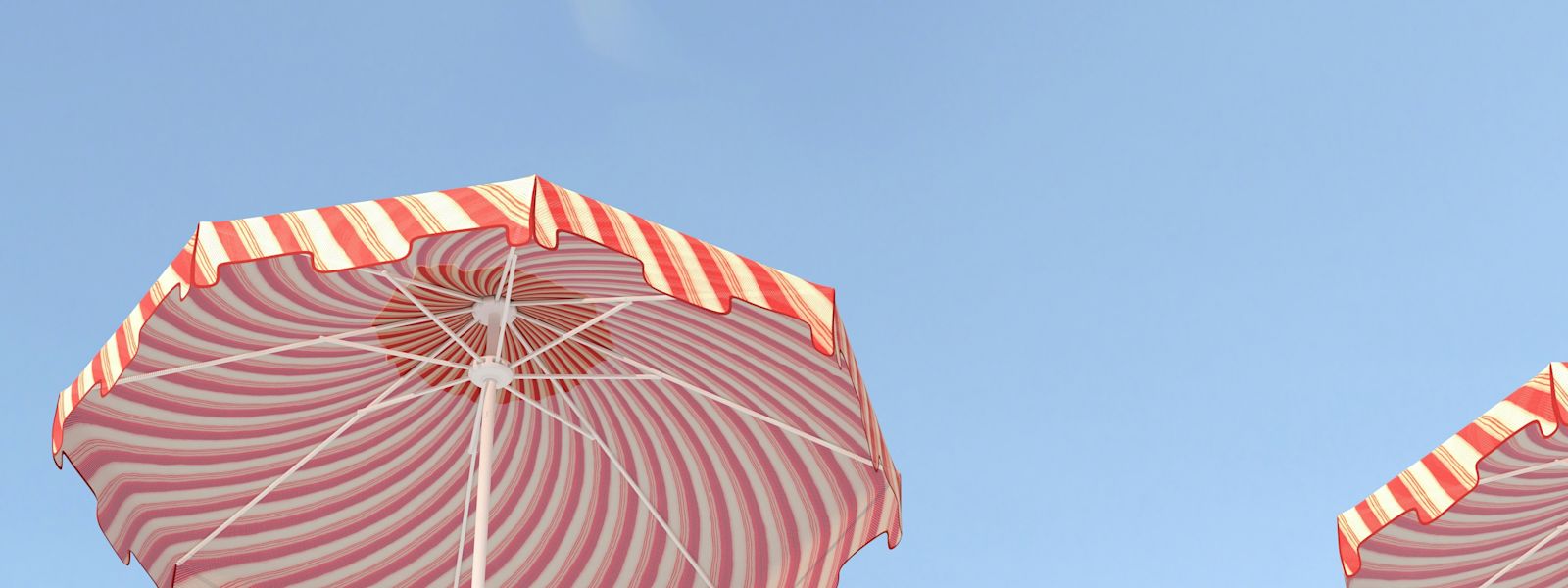 Orange and white striped beach umbrellas on a blue sky background.
