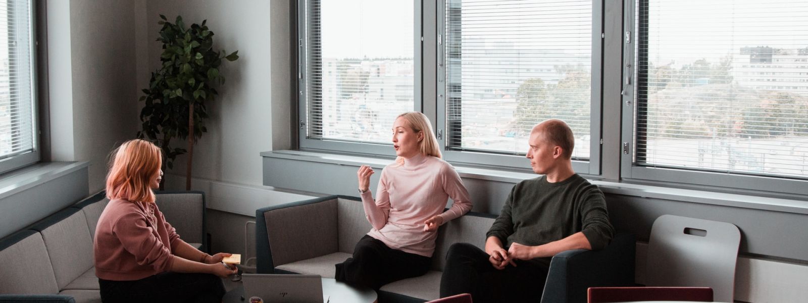 3 people deep in discussion (involving hand gestures) around some couches and a coffee table in a corporate environment.