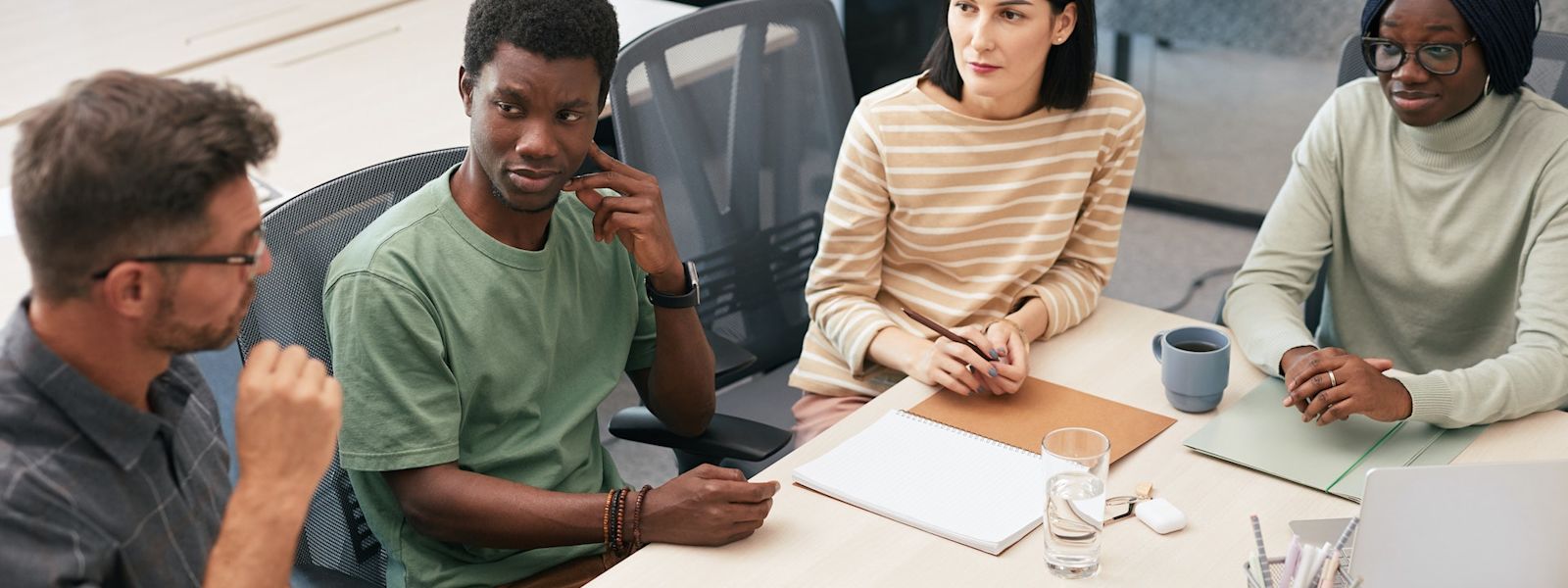 A group of 4 colleagues sitting next to each other around a table, deep in discussion with a laptop in the middle of the table.
