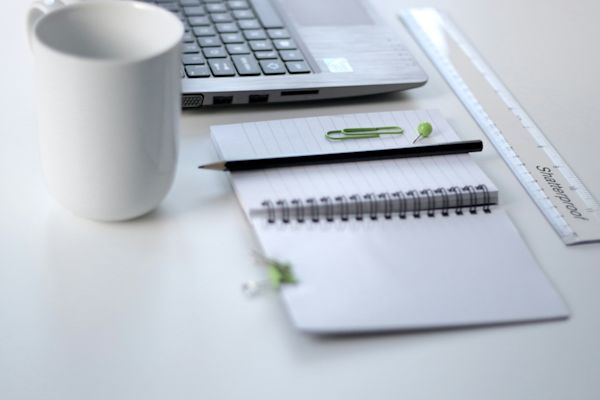 Coffee cup, notebook and laptop on a desk