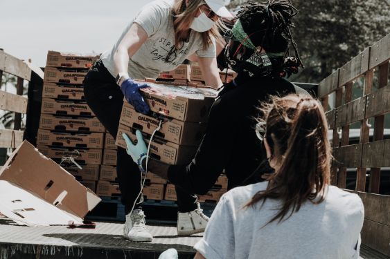 A volunteer is standing on the back of a truck, passing boxes of strawberries to other people.