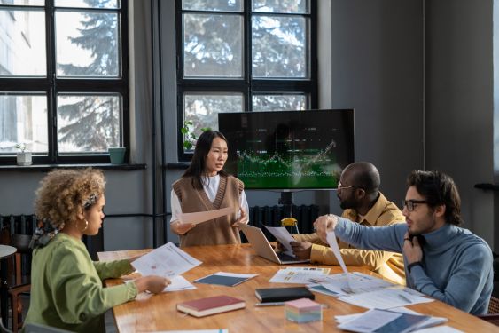 A group of accountants huddled around a desk, poring over paper charts.